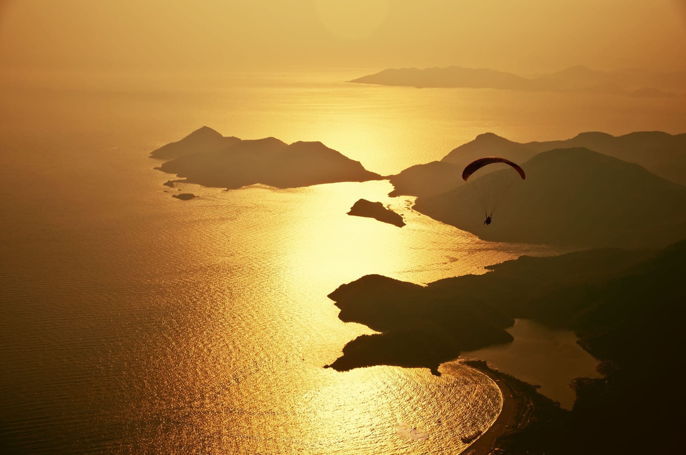 A paraglider over a golden sea at sunset